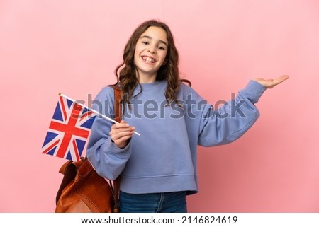Little girl holding an United Kingdom flag isolated on pink background extending hands to the side for inviting to come