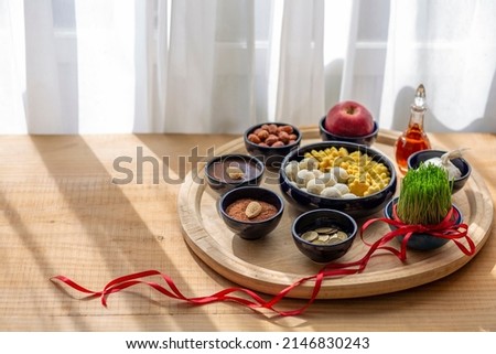 Nowruz festive table,Persian new year decoration,Tabletop with Haft-seen elements for Novruz: green wheat grass with red ribboncookie.pastry.Cultural feast.Traditional celebration of spring in March.