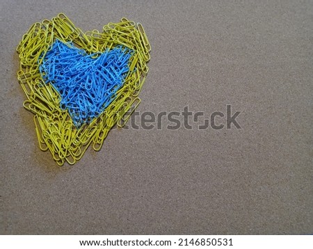 A brown background with yellow and blue paperclips signifying Ukraine being held together with love.