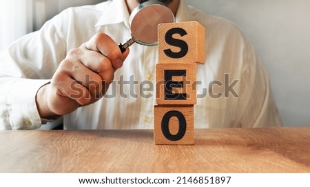 SEO inscription on the texture of wooden cubes. A business man holds a magnifying glass in his hand and examines the inscription on the cubes. An inscription on a financial.