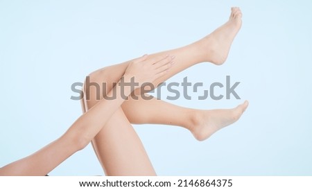 Horizontal medium shot of female legs. Young slim lying woman touches her leg on pale blue background | Leg care and unwanted hair removal concept Royalty-Free Stock Photo #2146864375