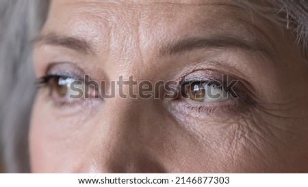 Close up cropped wrinkled front face view of attractive brown-eyed older woman staring into distance looking pensive and thoughtful. Eyes vision check up clinic ad services for older citizen concept Royalty-Free Stock Photo #2146877303