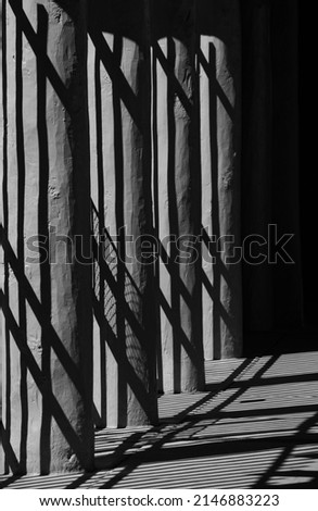black and white abstract of shadows cast onto wooden pillars and cement sidewalk on pathway in downtown Santa Fe New Mexico near the plaza vertical format room for type geometrical shapes and pattern