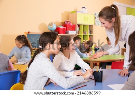boys and girls sitting and positive teacher helping drawing in classroom
