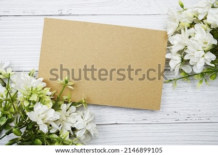 Empty paper card with white daisy flower flat lay on wooden background