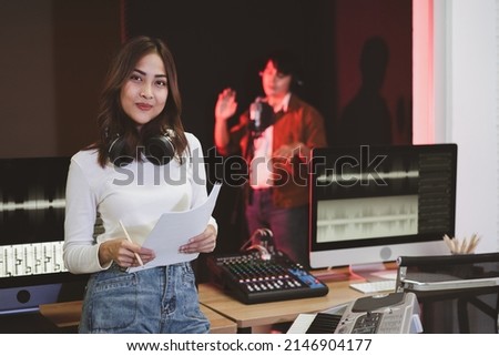 Asian producer woman in white shirt standing by sound mixing console. Happy female music composer artist with a man singer background  
 Royalty-Free Stock Photo #2146904177