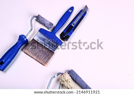 a set of blue construction tools for apartment renovation. rollers, brushes, stationery knife, measuring tape, paint bathon a beige background