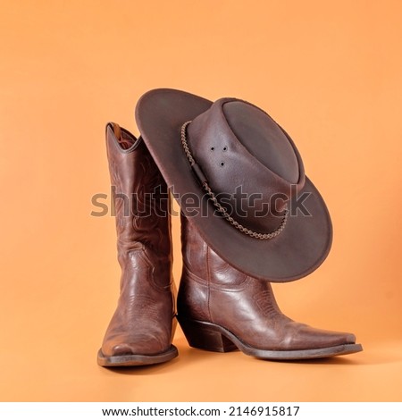 Two elegant classic boots and a leather cowboy stetson hat on an orange clay background. Ranger cowboy concept on a ranch in america usa texas.
