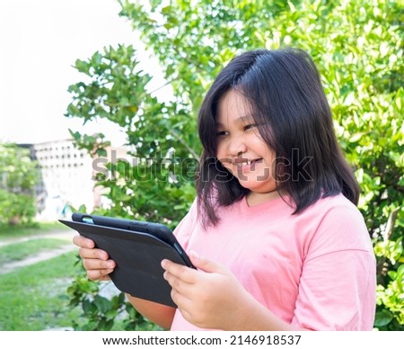 Portrait fat girl beautiful cute teenager woman Asian standing inside park garden house, wearing pink shirt. Happy smile looking with tablet mobile in holding hand after studying education online 