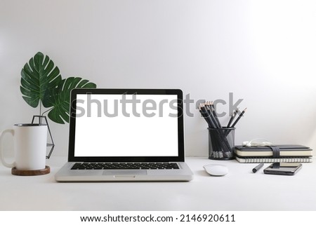 Mockup laptop with empty display, coffee cup, books and picture frame on white table.	