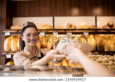 Beautiful woman working in bakery shop and selling fresh tasty pastry to the customer. Royalty-Free Stock Photo #2146924417
