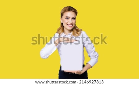 Cheerful smiling business woman in white confident clothing showing empty mock up signboard. Success and advertising concept. Copy space place for some text or imaginary. Yellow background.