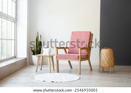 Stylish pink armchair and table with wicker lamp in interior of room Royalty-Free Stock Photo #2146935001