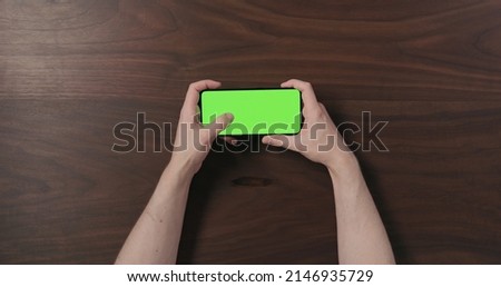 Top view man hand use smartphone with green screen over black walnut wood table, wide photo
