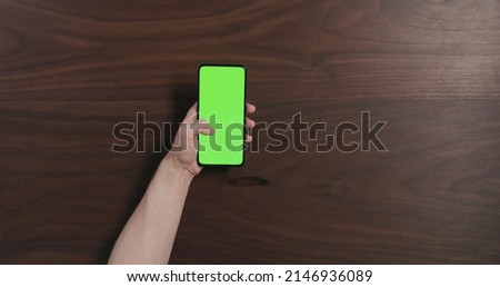 Top view man hand using smartphone with green screen over black walnut wood table, wide photo
