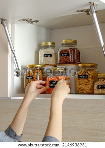 Young Asian woman stacks glass jars with horns in kitchen cabinet. Storage of bulk products. Zero waste. Vegetarian woman. Conscious consumption. Royalty-Free Stock Photo #2146936931