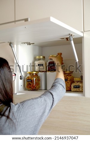 Young Asian woman stacks glass jars with horns in kitchen cabinet. Storage of bulk products. Zero waste. Vegetarian woman. Conscious consumption. Royalty-Free Stock Photo #2146937047