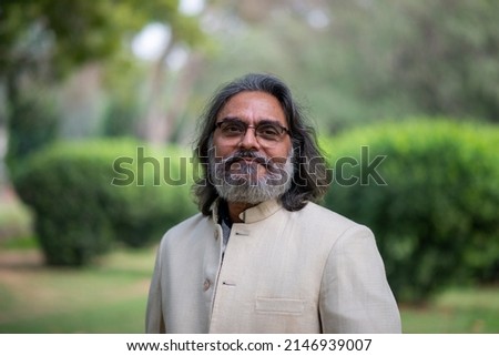 A grey bearded handsome man in band gala traditional handmade woolen coat posing for picture in a public park. 