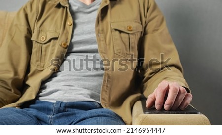 Man in mustard jacket sits in soft armchair tapping fingers on armrest against grey wall at home. Freelancer takes break after hard work closeup Royalty-Free Stock Photo #2146954447