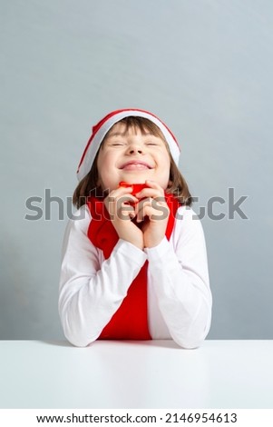 Holidays and Christmas Ideas. Dreaming Winsome Caucasian Female Girl in Santa Hat and White Shirt Holding Tiny Red Gift Box in Front of Face. Vertical Image Composition