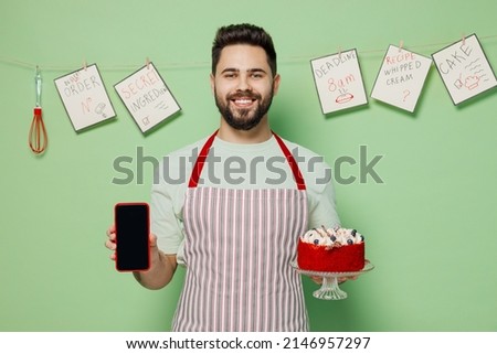 Young male chef confectioner baker man in apron hold birthday sweet dessert cake mobile cell phone with blank screen workspace area isolated on plain pastel light green background Cooking food concept