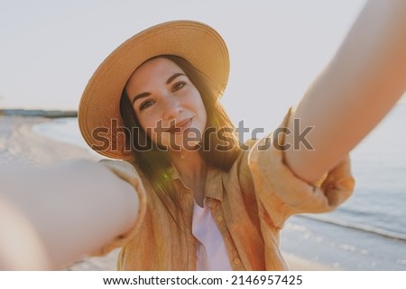 Close up attractive young woman 20s in straw hat shirt summer casual clothes do selfie shot mobile cell phone outdoors at sunrise sun dawn over sea background People vacation lifestyle journey concept