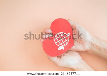 world with leaf icon on red heart paper shape in hand on sweet orange background for saving environment, save clean planet, ecology concept. Card for World Earth Day