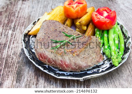 thick juicy portions of grilled fillet steak served with tomatoes and roast vegetables on an old wooden board 