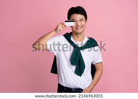 Smiling handsome young man in casual clothes posing alone on a pink wall photo studio background. He holds an eye cover with a bank card.
