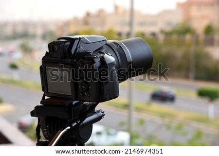 A digital camera fixed on a tripod for time lapse footage and video recording with a blurred top view of a city street and buildings, camera is pointed to the skyline filming the sun, sky and clouds