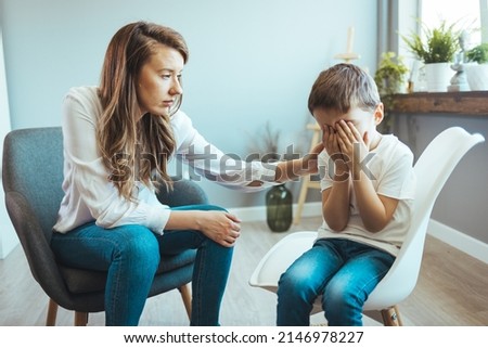 Children need help. Upset little boy crying in psychologist's office unable to control emotions, sharing problems and traumas, professional psychotherapist comforting kid, side view