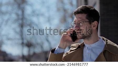 Young stylish man in glasses talking on cellphone at the city street. Businessman answering telephone call.