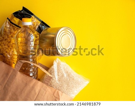 A paper bag with crisis food stocks for the period of the war. Buckwheat, pasta, oatmeal and sunflower oil on yellow. Food Delivery, Donation, Coronavirus, Quarantine, War. Place for text. Royalty-Free Stock Photo #2146981879