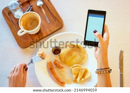 Close up of women's hands holding smartphone with blank copy space screen. Watching video on mobile phone during breakfast.