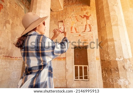 Travel blogger girl takes pictures on a smartphone at the famous Hatshepsut temple in the ancient city of Luxor in Egypt.