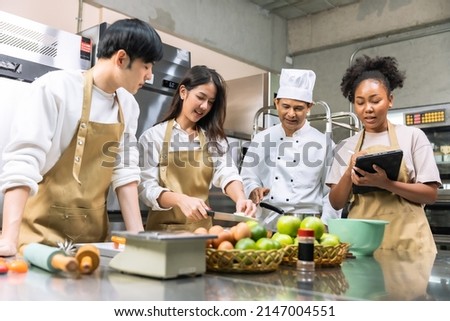 Cooking  course , senior Asian male chef in cook uniform teaches young asian and african american people cooking class students to prepare, mix ingredients for pastry foods, in restaurant stainless  Royalty-Free Stock Photo #2147004551