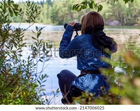 Young woman looking through binoculars at birds on the lake. Birdwatching, zoology, ecology. Research in nature, observation of animals Ornithology autumn bird migration selective focus, soft focus.  Royalty-Free Stock Photo #2147006025