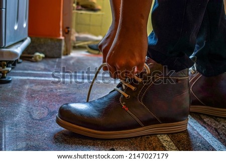 Stock photo of Indian man wearing dark brown color shoe and tying shoe lace, getting ready for his office. Picture captured under natural light at Bangalore, Karnataka, India. focus ob object.