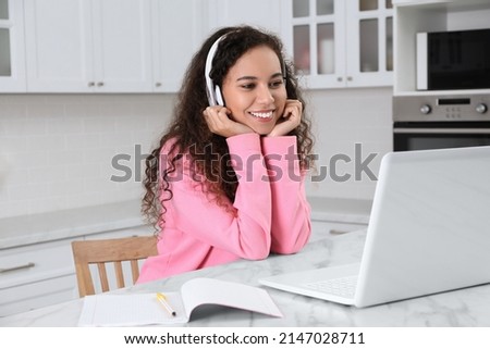 African American woman with modern laptop and headphones studying in kitchen. Distance learning