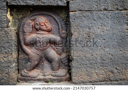Stock photo of Ancient ruined archeological sculpture of hindu god hanuman engraved on gray stone wall. Picture captured during sunny day at Kolhapur , Maharashtra, India. focus on object.