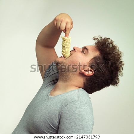 For my next trick I will make these chips disappear. Studio shot of an overweight man shoving a stack of chips down his throat. Royalty-Free Stock Photo #2147031799