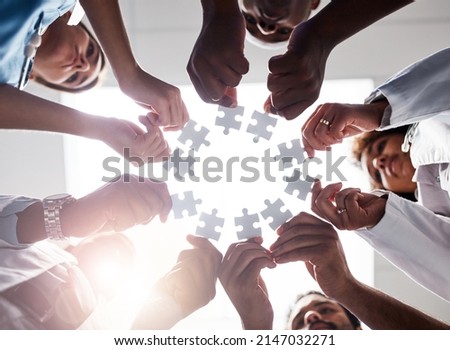 Everyone plays their part here. Low angle shot of a group of doctors forming a huddle while each holds a puzzle piece inside of a hospital. Royalty-Free Stock Photo #2147032271