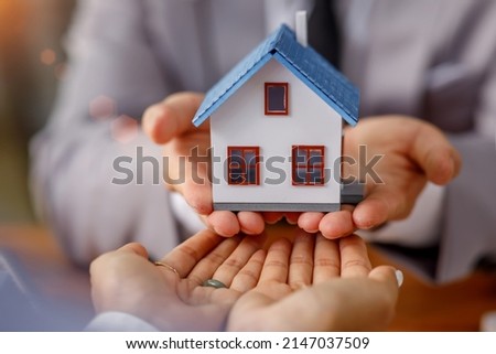 Real estate brokerage agent Deliver a sample of a model house to the customer, mortgage loan agreement Making lease and buying a house And contract home insurance concept  Royalty-Free Stock Photo #2147037509