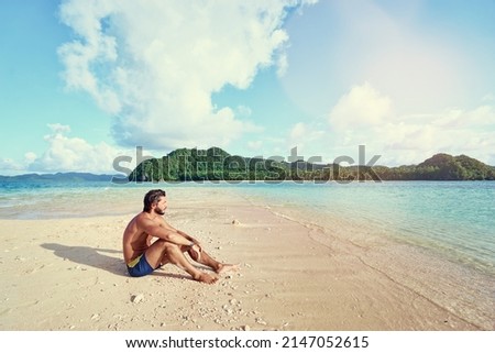 Tropical vacation. Relaxed young man sitting on the sand beach enjoying the island view. Royalty-Free Stock Photo #2147052615