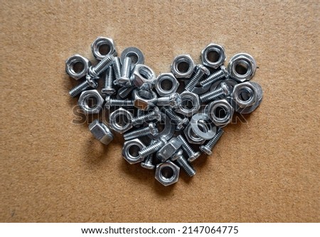 Heart shaped arrangement of the tools and screw nuts on brown paper background from a top view.