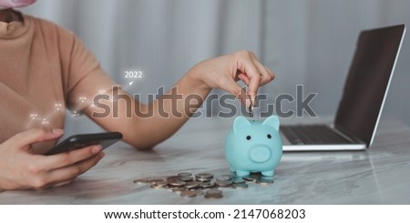 money saving concept Close your hands and put coins in the piggy bank for saving money. A smart woman holds a silver coin and prepares to put it in a piggy bank. with annual graph Royalty-Free Stock Photo #2147068203