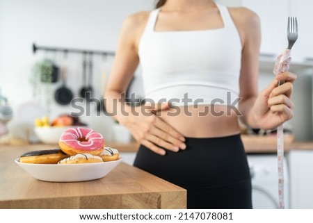 Asian beautiful young girl hungry and want to eat donut in kitchen. Attractive woman wear sport cloth feeling famished after exercies and pick up junk food unhealthy to eat, Food and health concept. Royalty-Free Stock Photo #2147078081