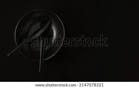 Black plate in the japanese style with fork and knife, table setting. Flat lay. Black background, top view with copy space. Minimalist breakfast idea in black color.