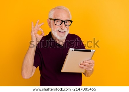 Photo of cheerful mature man show fingers okey symbol approve good tablet app isolated over yellow color background