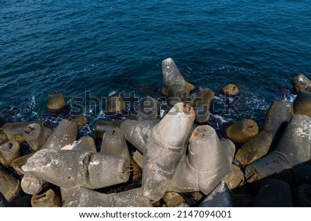 Large tetrapod concrete blocks lies on breakwater by blue sea water in a sunny day. Calm water. Coastal management theme. Royalty-Free Stock Photo #2147094001
